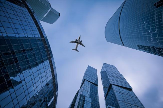 Photo of an airplane above the glass office buildings 