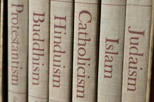 Book spines listing major world religions &#8211; Judaism, Islam, Catholicism, Hinduism, Buddhism and Protestantism. The focus is on the word, Catholicism 
